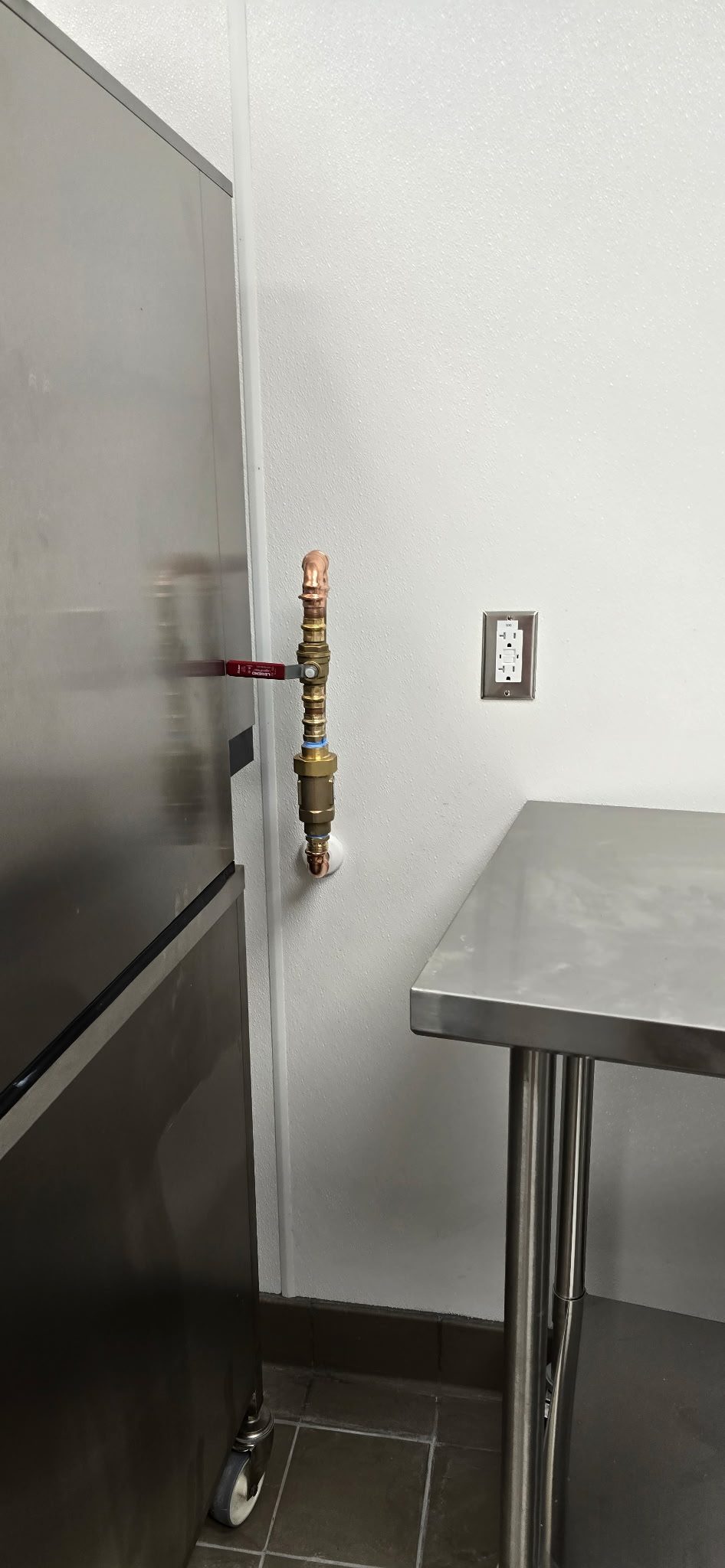 Copper supply line drop fitted with a brass ball valve shutoff on a kitchen wall beside stainless equipment