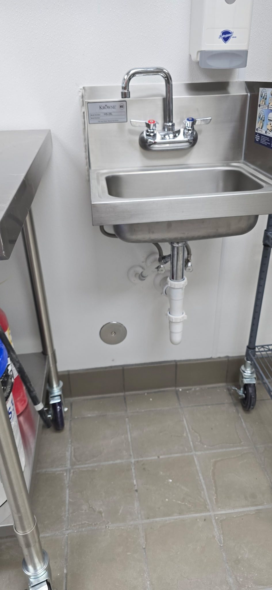 Stainless steel hand sink with a gooseneck faucet and soap dispenser installed in a commercial kitchen