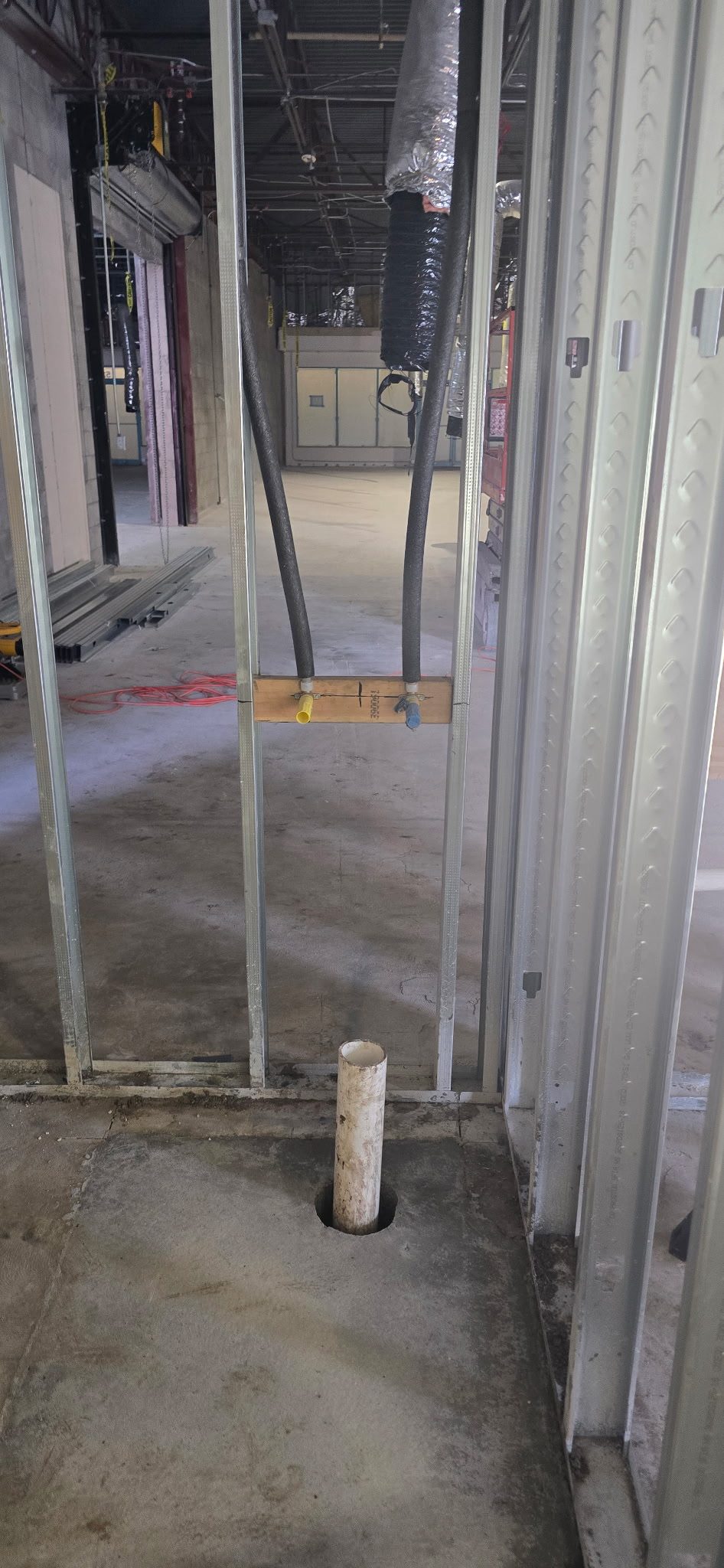 PVC drain stub-up protruding from a concrete slab inside metal stud framing on a commercial job site