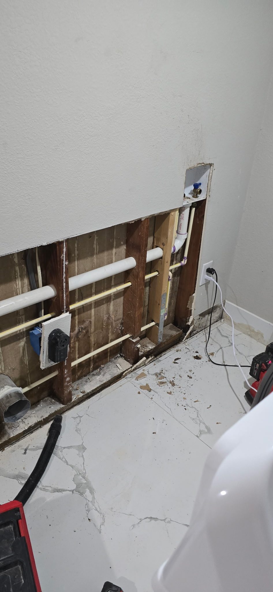 Open interior wall with the drywall removed, showing new white water lines run horizontally between the wall studs