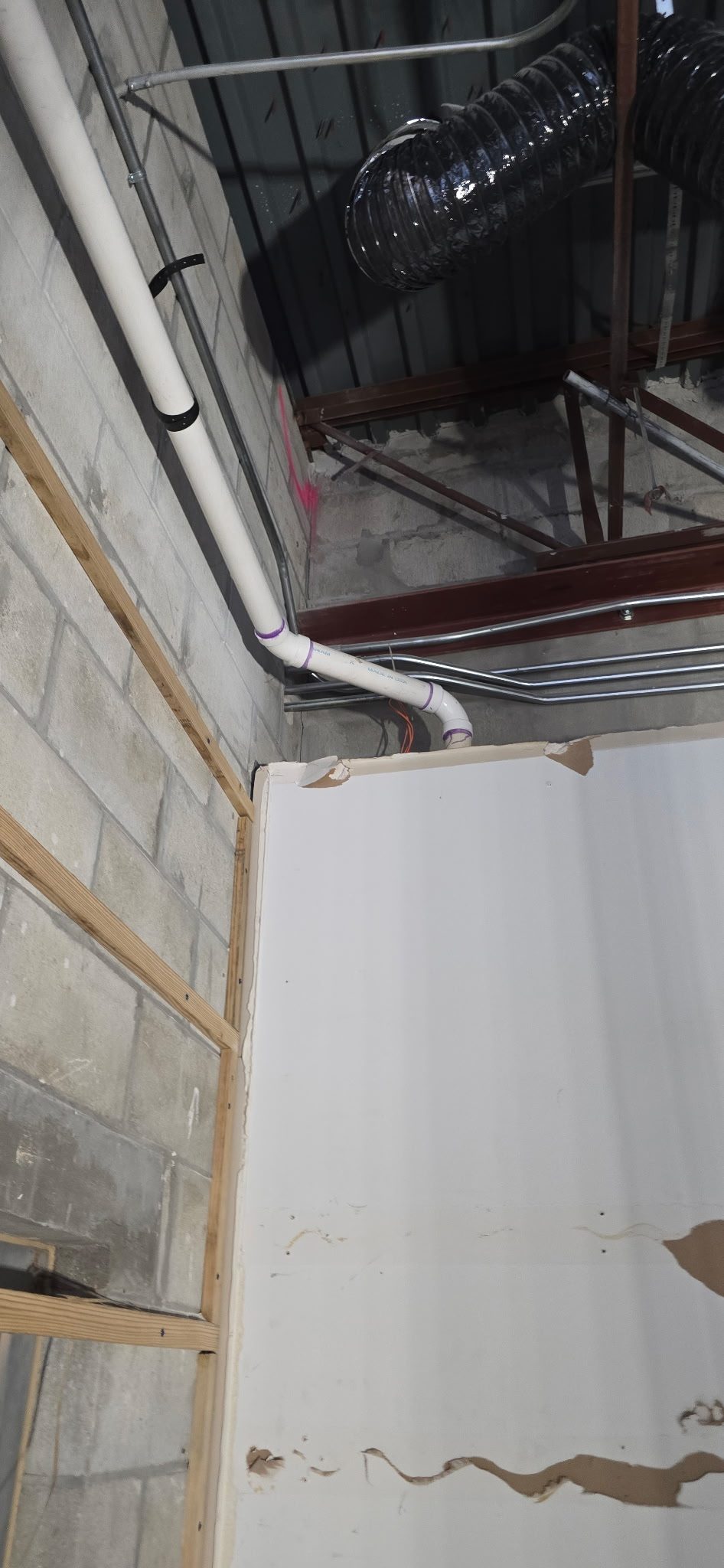 PVC drain and vent piping routed along a concrete block wall above a partially finished ceiling