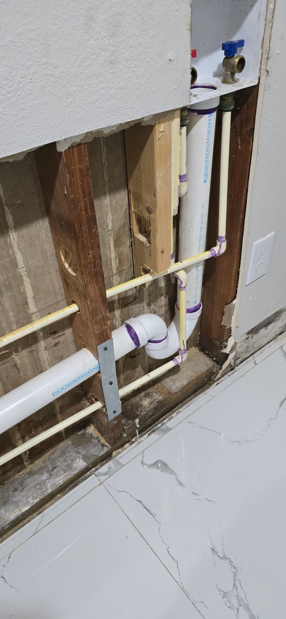 Close-up of new PVC drain piping and water supply lines with a shutoff valve, strapped to studs inside an open wall