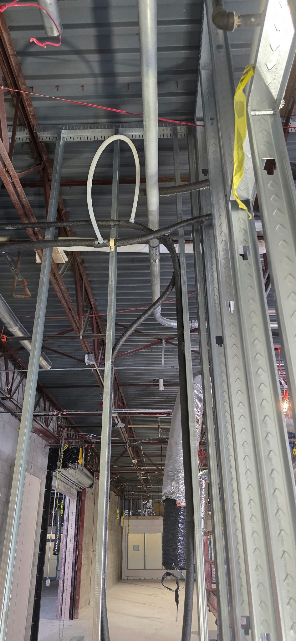 Water piping and flexible line routed overhead through steel framing above a commercial ceiling