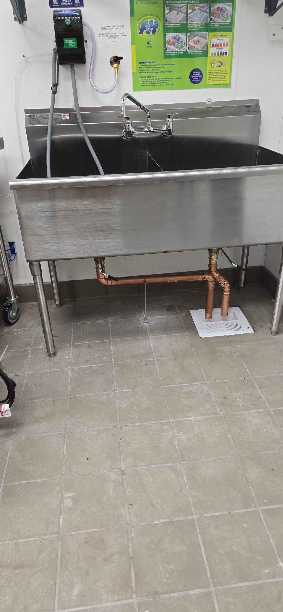 Three-compartment stainless steel kitchen sink with new copper drain lines running down to a floor sink