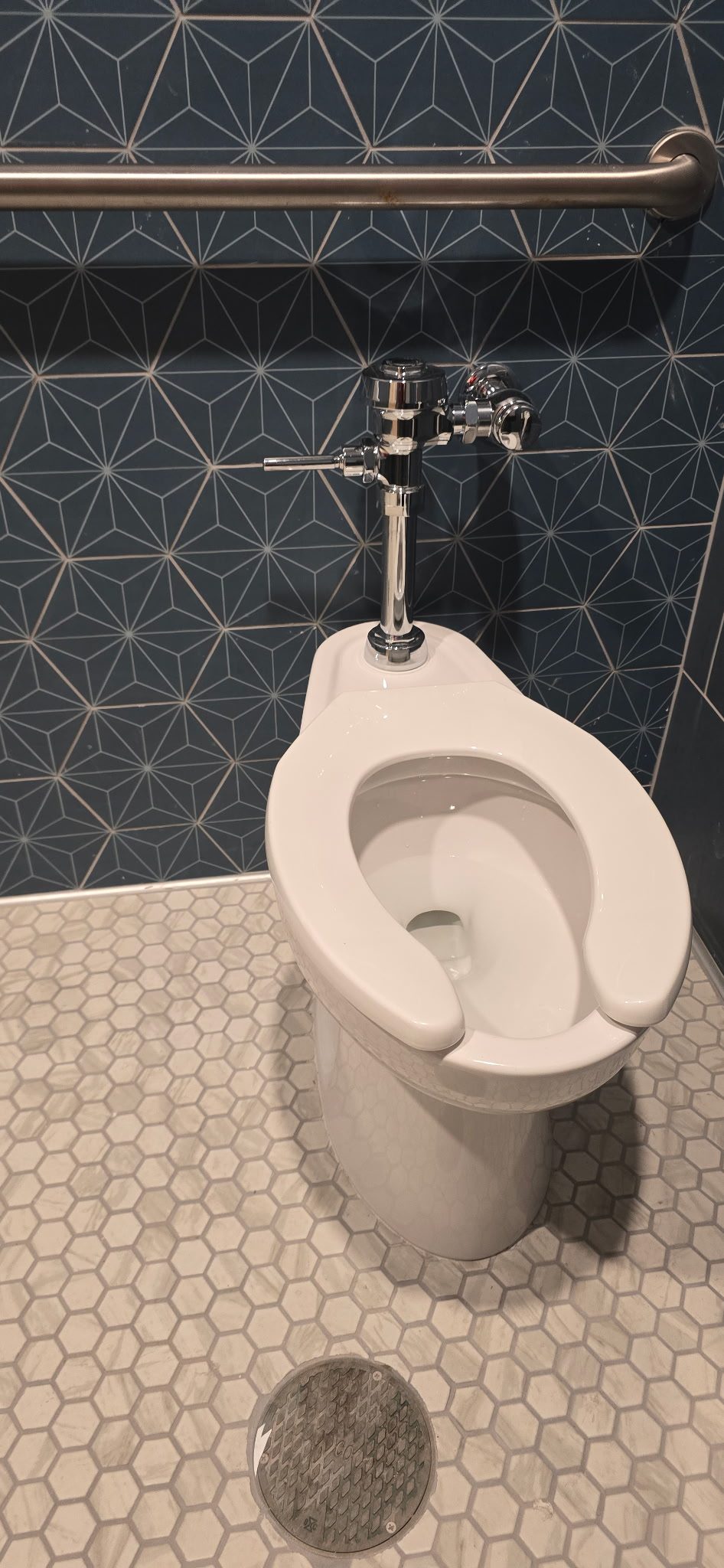 Floor-mounted commercial toilet with a chrome flushometer valve installed in a tiled restroom stall